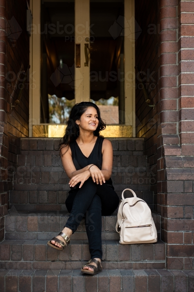 young woman sitting on stairs outside apartment entrance - Australian Stock Image