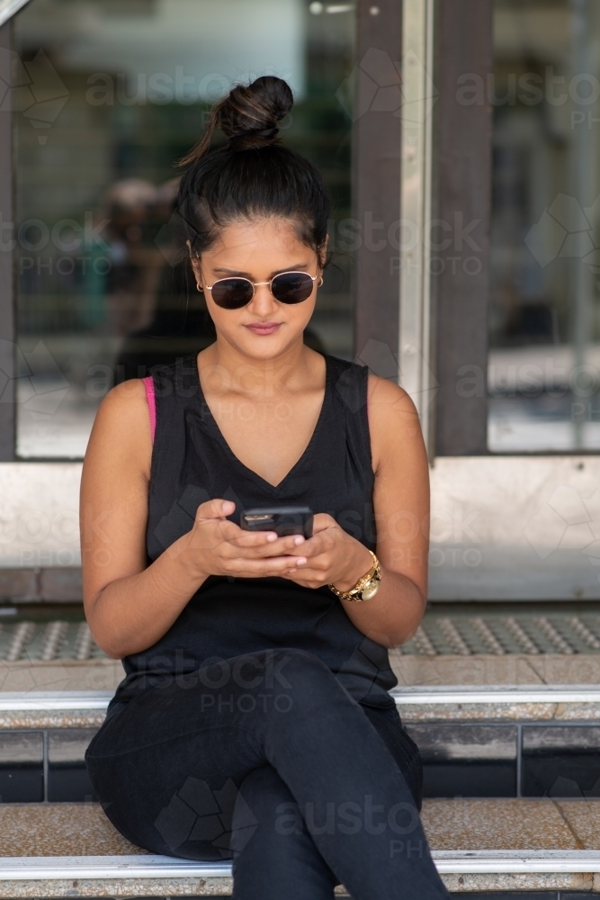 young woman sitting on stairs using phone - Australian Stock Image