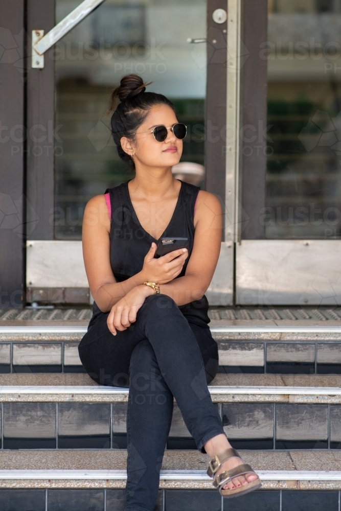 young woman sitting on stairs using phone - Australian Stock Image