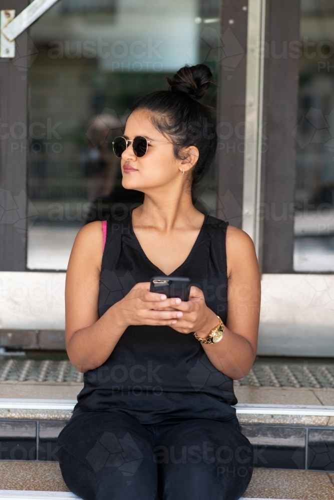 young woman sitting on stairs using phone - Australian Stock Image