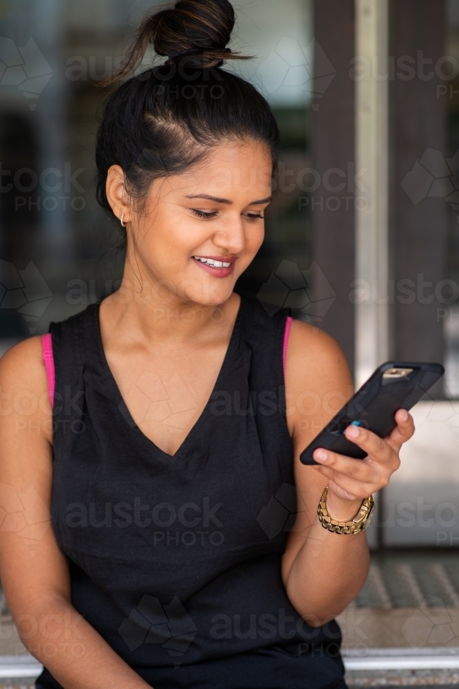 young woman sitting on stairs using phone - Australian Stock Image