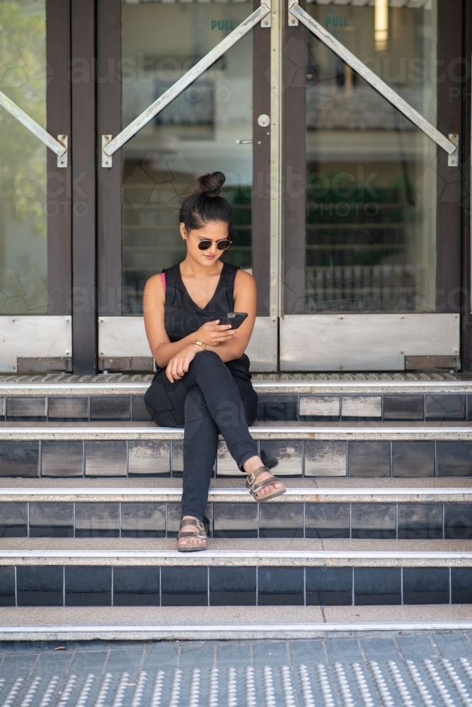 young woman sitting on stairs using phone - Australian Stock Image