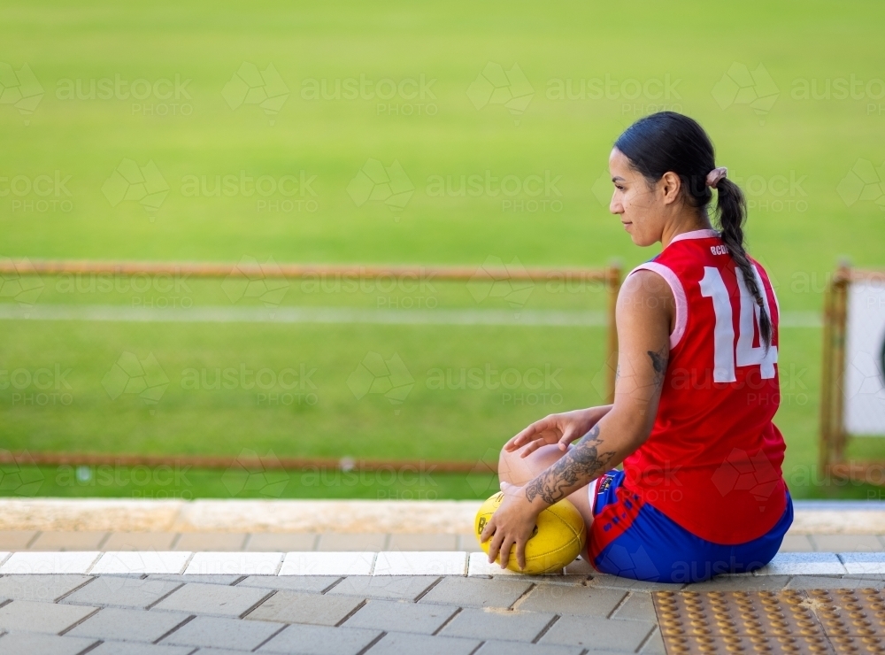 young woman sitting with football wearing football uniform - Australian Stock Image