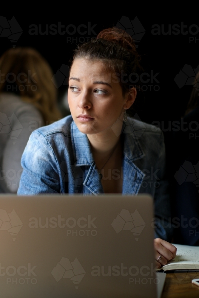 Young woman sitting with laptop staring out window with a concerned expression - Australian Stock Image