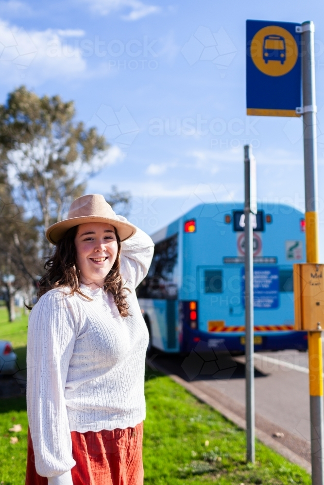 Young woman smiling beside public transport bus stop sign - Australian Stock Image