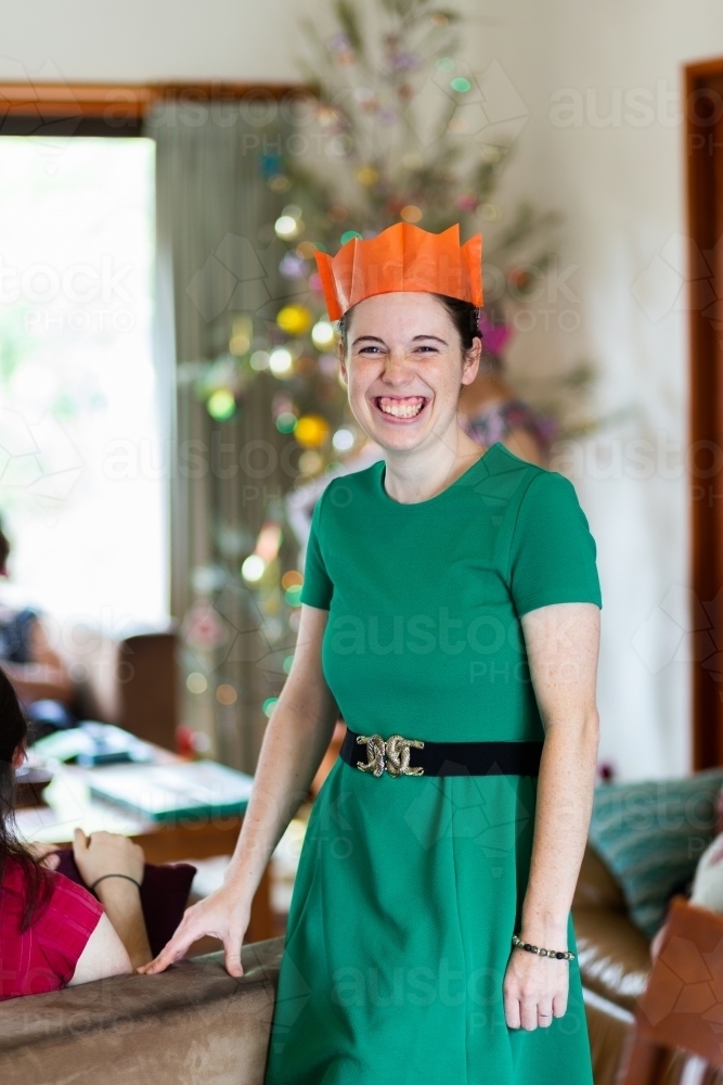 Young woman smiling celebrating Christmas day wearing paper crown - Australian Stock Image