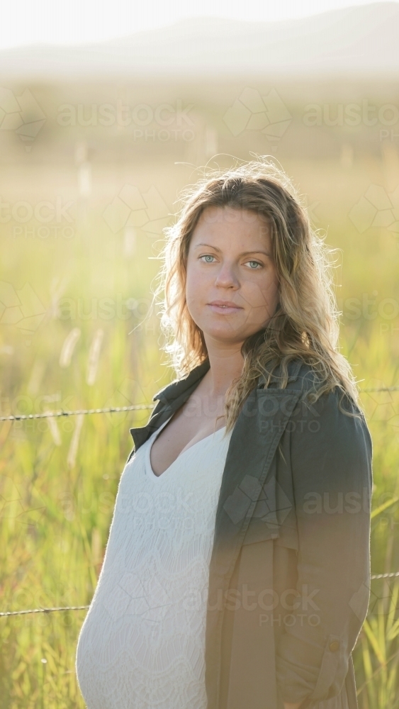 Young woman standing in field with sunflare behind : Austockphoto Young woman standing in field with sunflare behind - Australian Stock Image