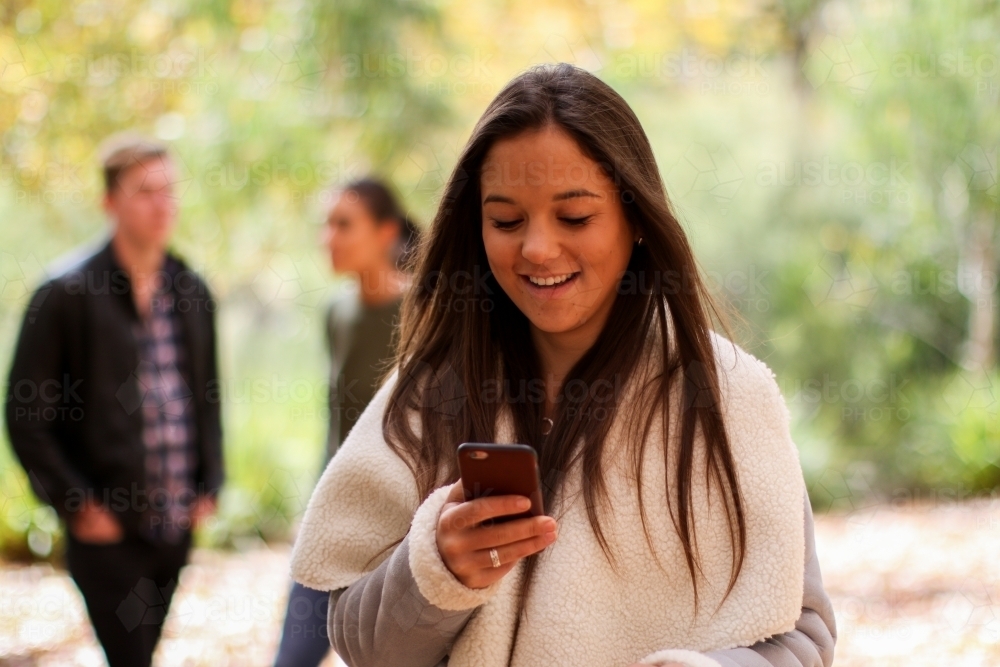 Young woman standing in front of a group of friends using a mobile phone - Australian Stock Image