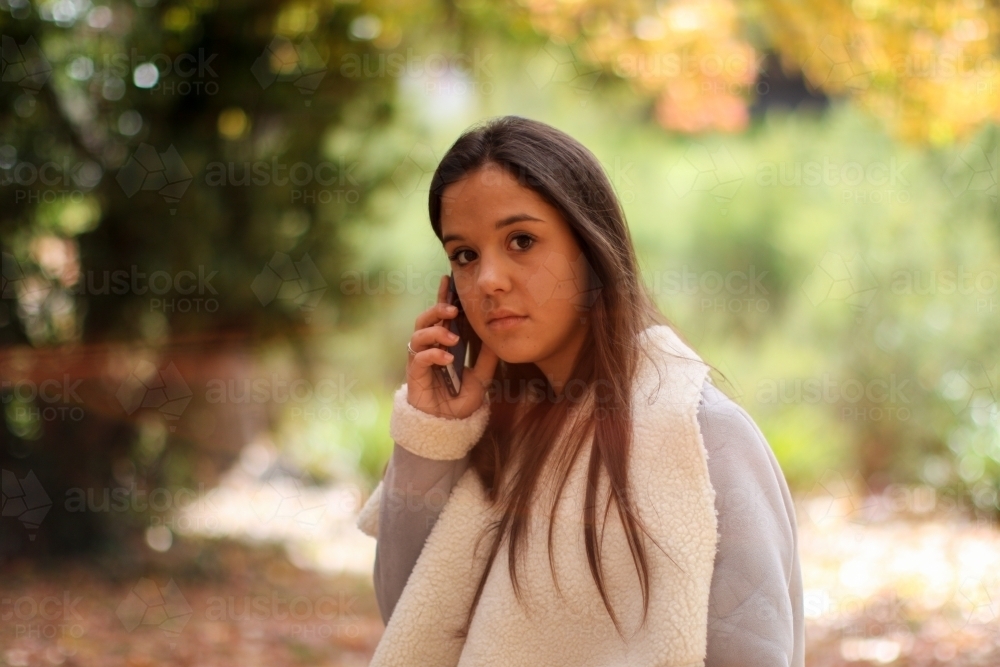 Young woman standing in the park using a mobile phone - Australian Stock Image
