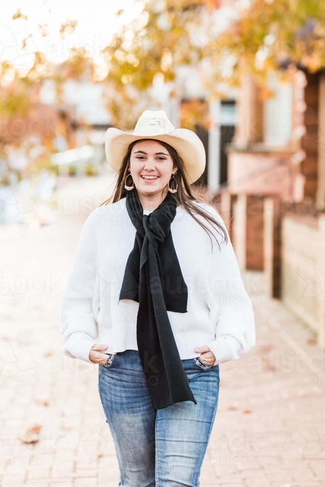 Young woman standing on street with hands in pockets smiling - Australian Stock Image