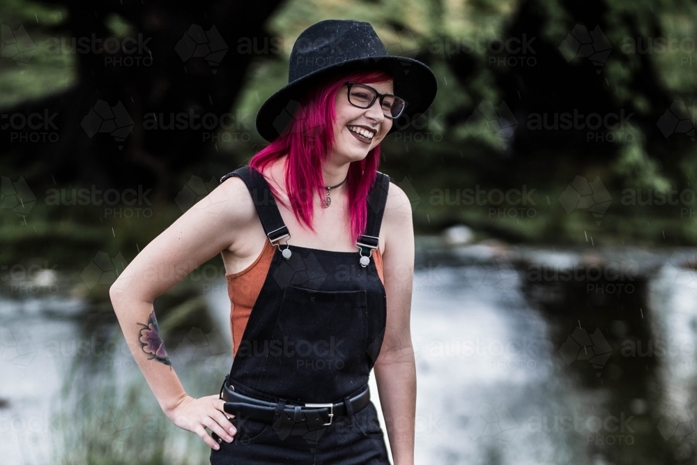 Young woman standing with hand on hip near water laughing - Australian Stock Image
