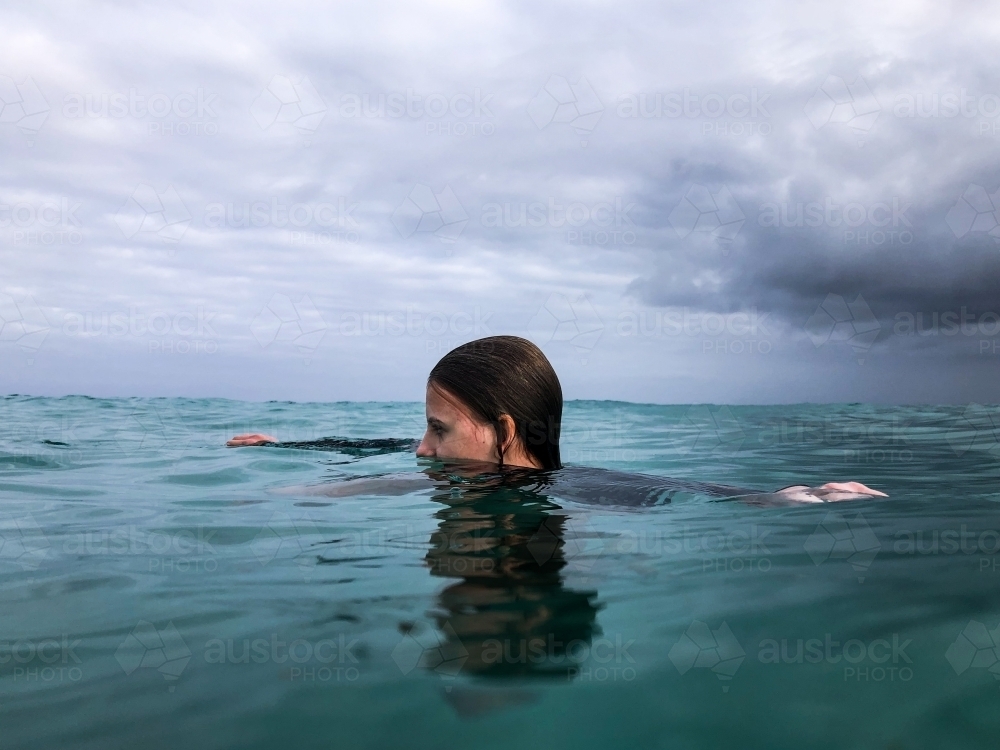 Young woman swimming in ocean on overcast day - Australian Stock Image