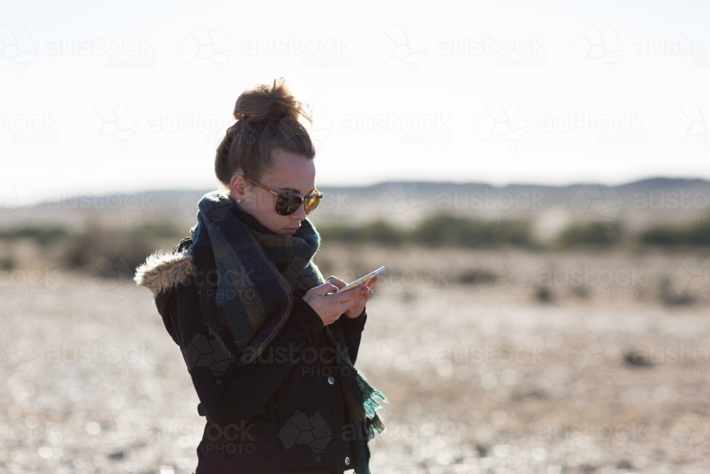 Young woman texting on smartphone in outback setting - Australian Stock Image