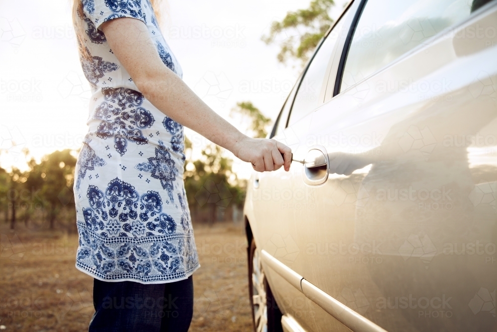 Young woman unlocking car on sunlit afternoon - Australian Stock Image