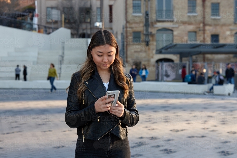 Young woman using mobile phone wearing leather jacket - Australian Stock Image
