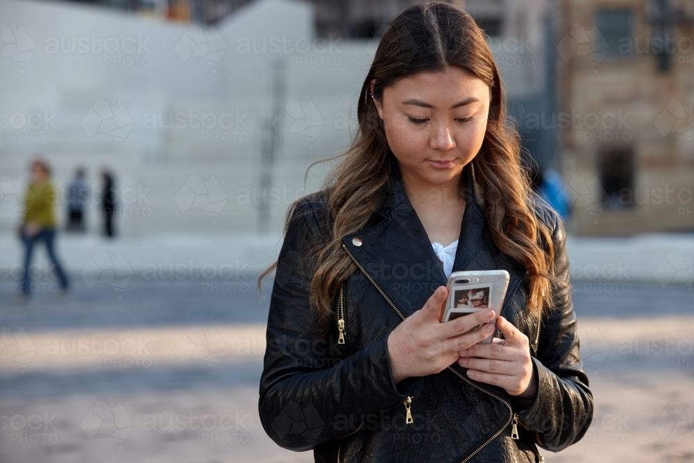 Young woman using mobile phone wearing leather jacket - Australian Stock Image