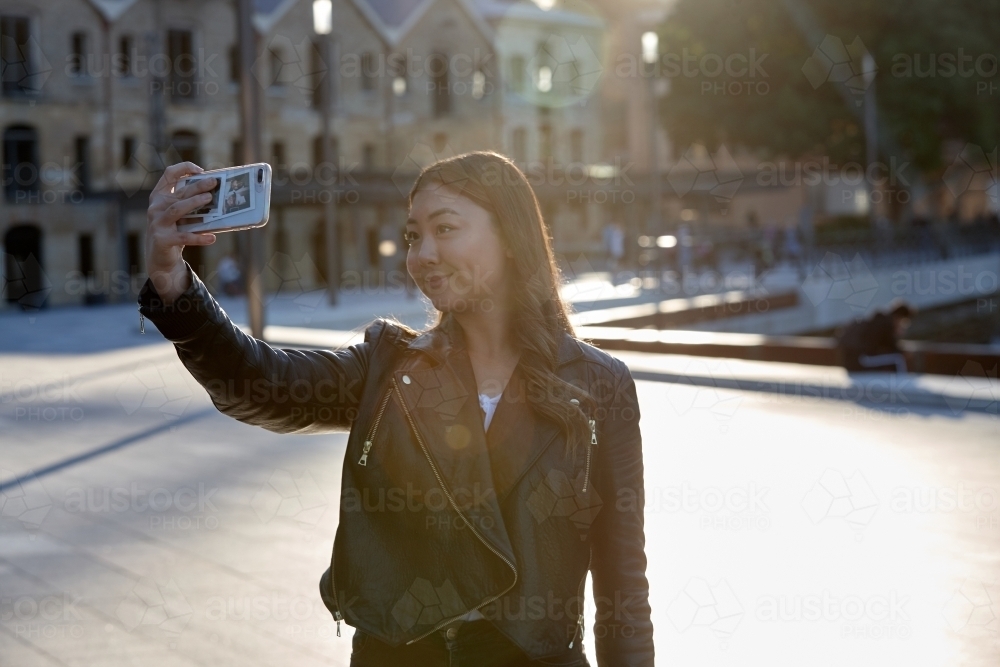 Young woman using mobile phone wearing leather jacket - Australian Stock Image