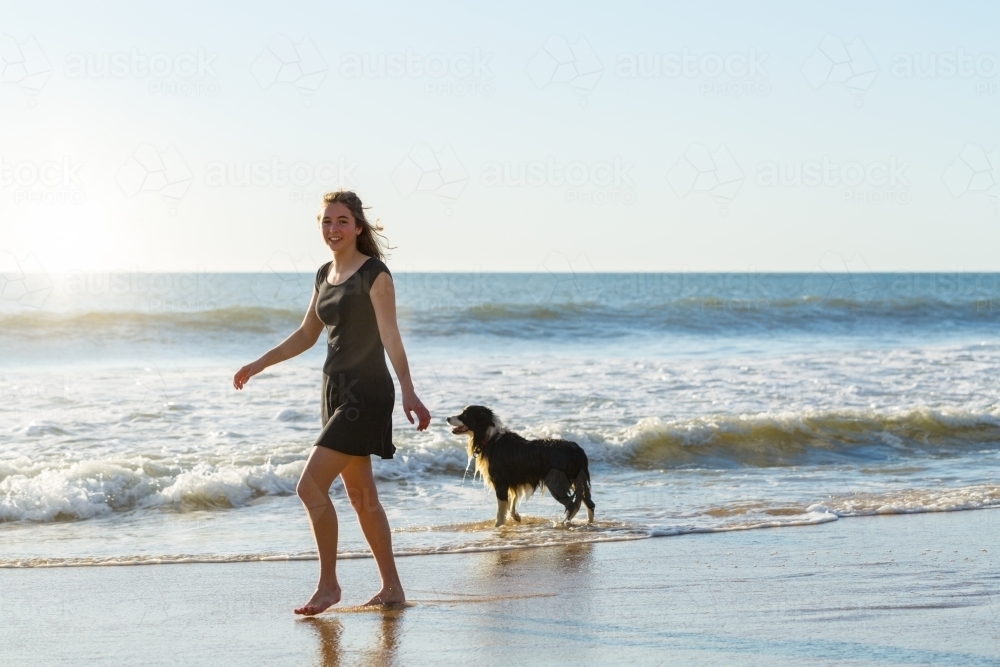 Young woman walking along beach with border-collie dog - Australian Stock Image