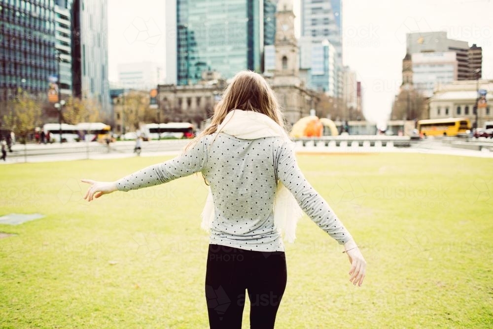 Young woman walking away on grass in the city - Australian Stock Image