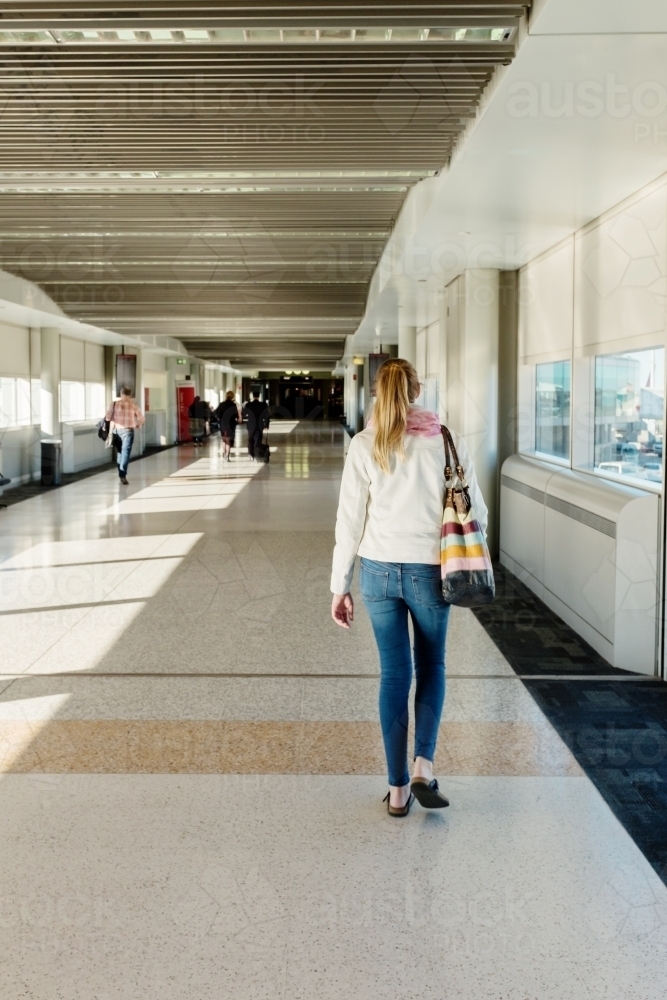 young woman walking down airport terminal corridor - Australian Stock Image