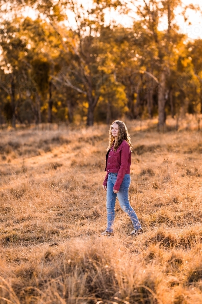 Young woman walking through paddock in golden light - Australian Stock Image
