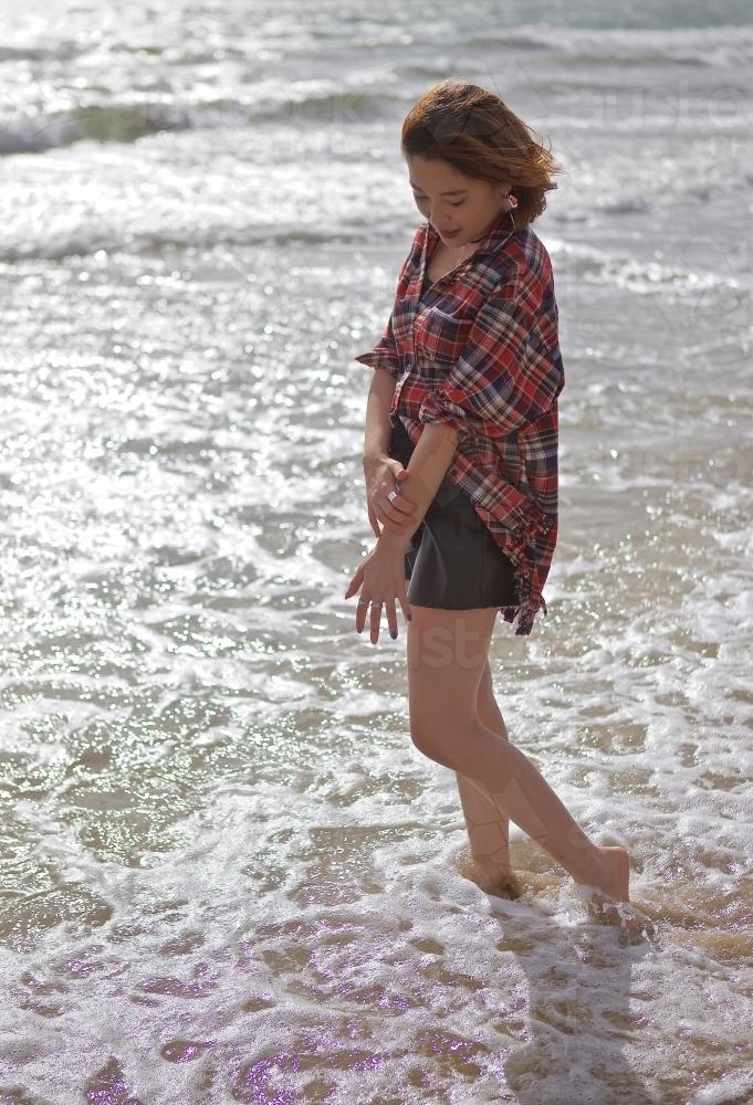 Young woman walking through the shallow waves on the beach - Australian Stock Image