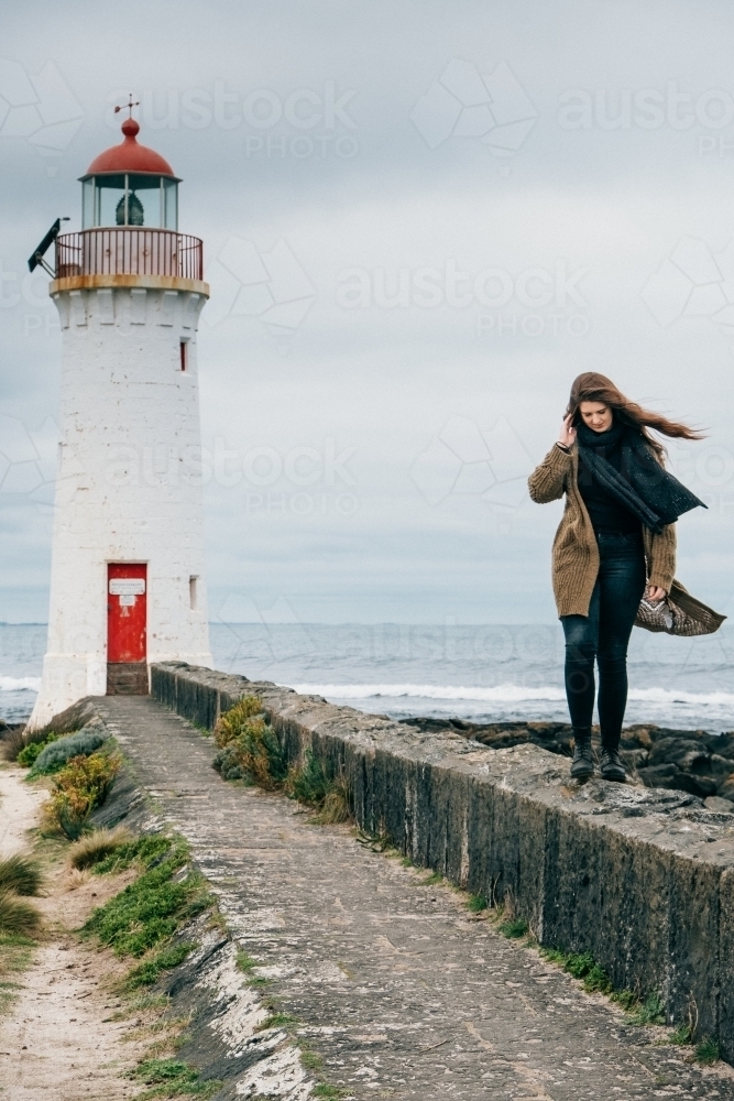 Young woman walks along the wall in front of lighthouse. - Australian Stock Image