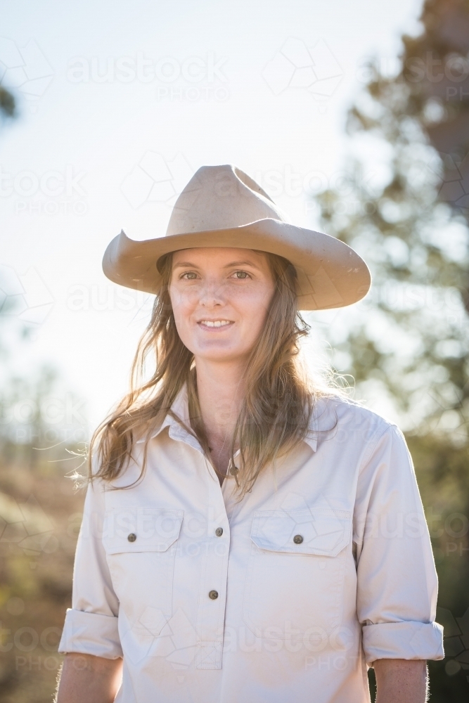 Young woman wearing akubra hat standing on family farm in drought - Australian Stock Image