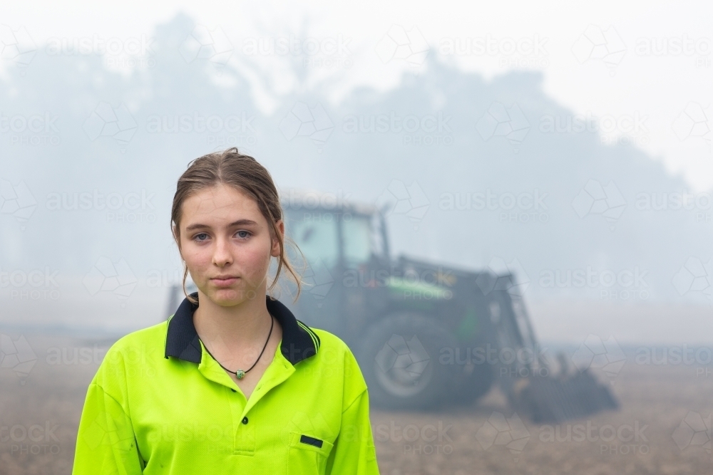 Young woman wearing hi-vis in front of tractor - Australian Stock Image