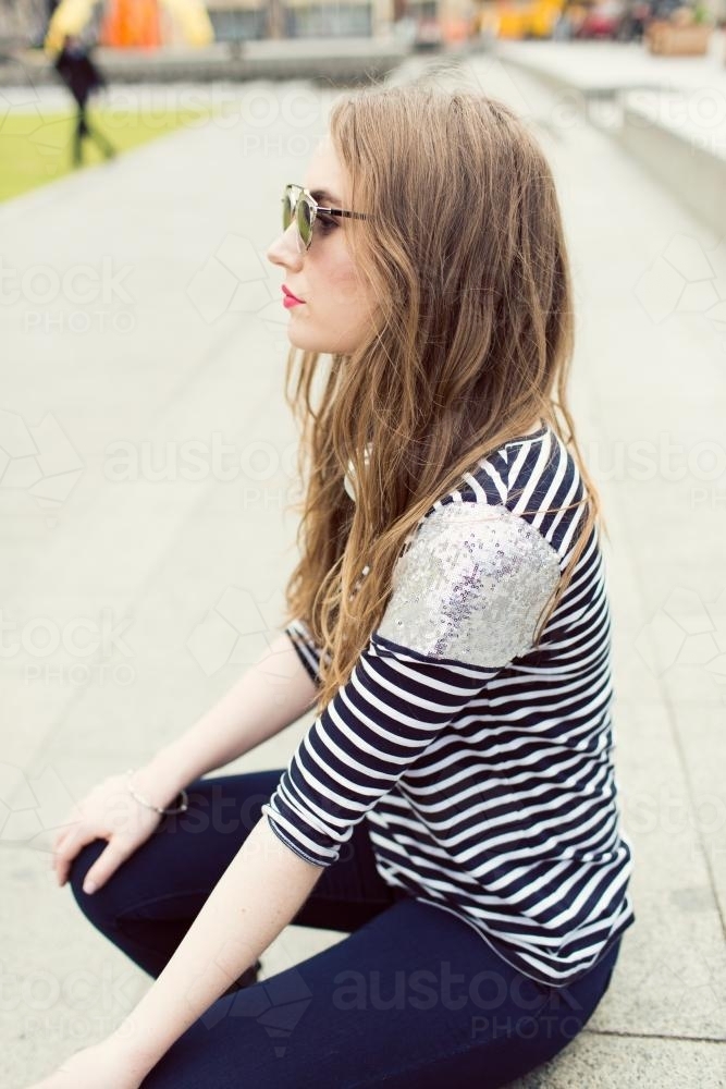 Young woman wearing sunglasses sitting down - Australian Stock Image