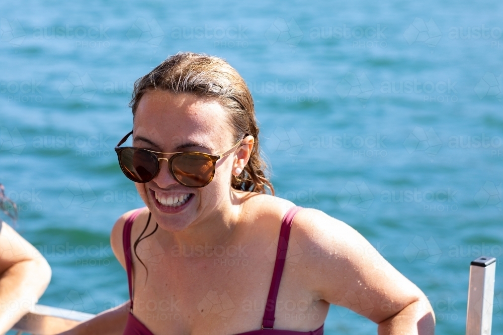 young woman wearing sunglasses with wet hair and blue water in the background - Australian Stock Image