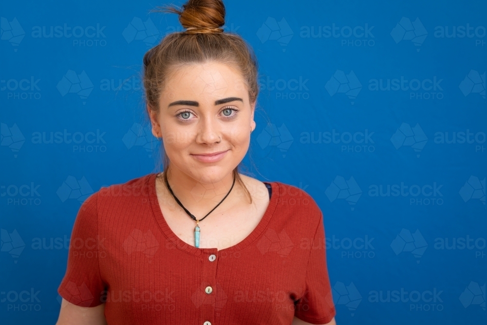 young woman with bun looking at camera against blue background - Australian Stock Image