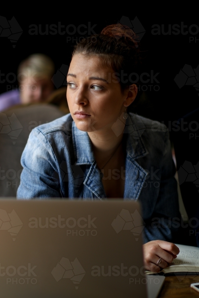 Young woman with concerned expression sitting at a desk behind a laptop - Australian Stock Image