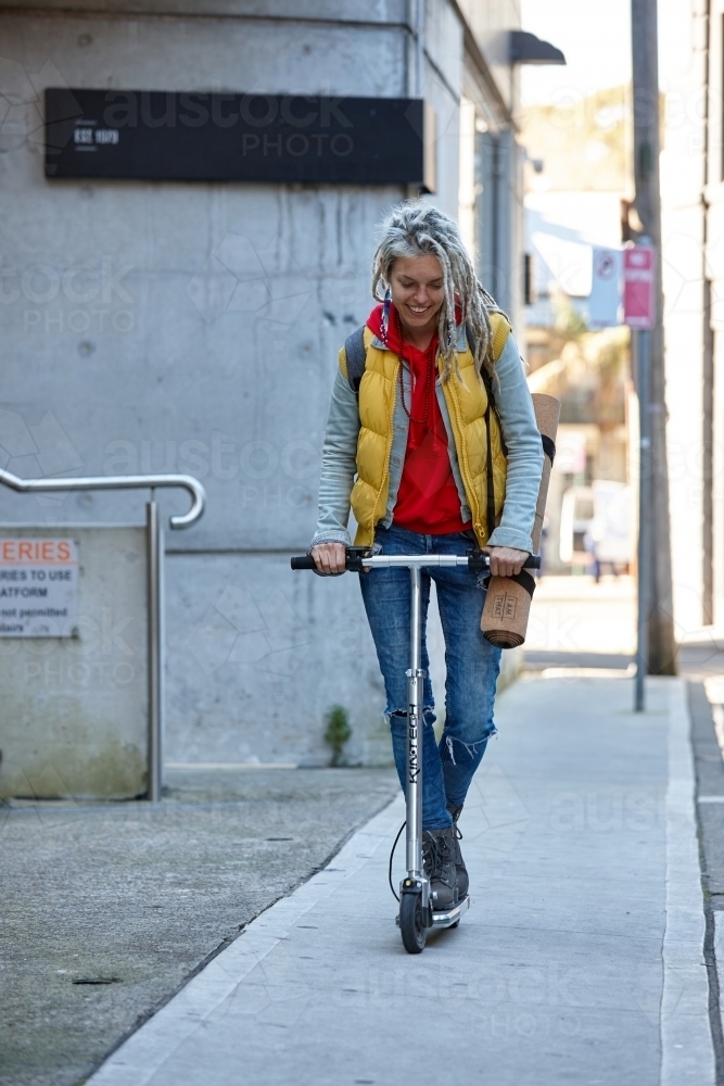Young woman with dreadlocks riding electric scooter - Australian Stock Image