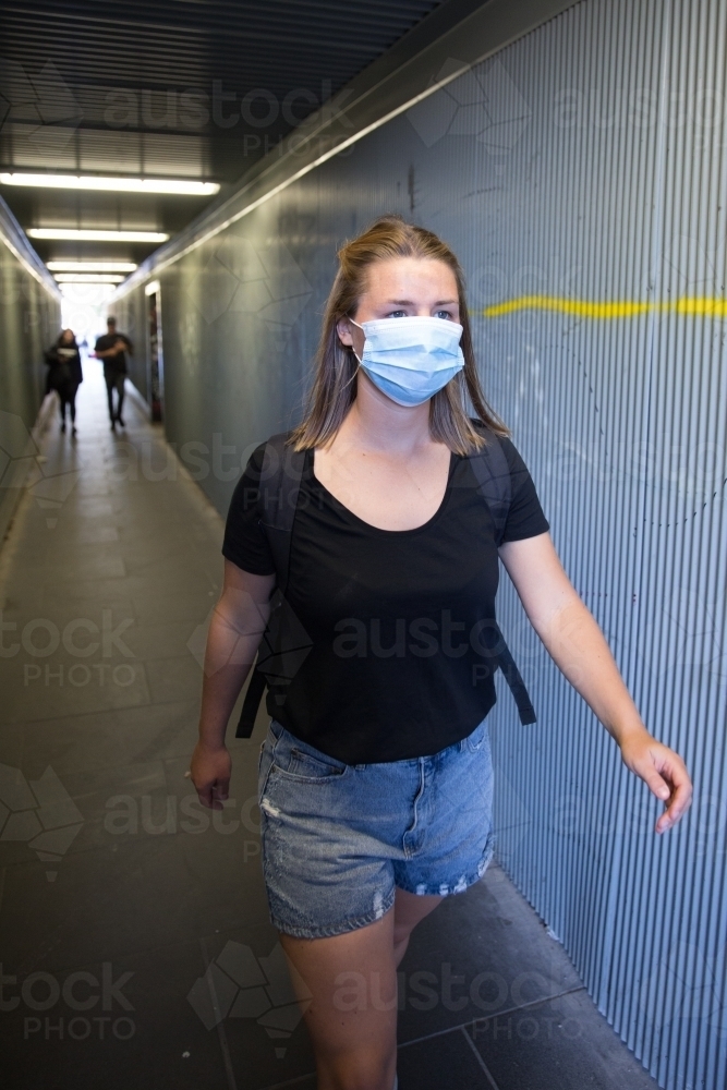 Young Woman with Face Mask Walking Through City Tunnel - Australian Stock Image