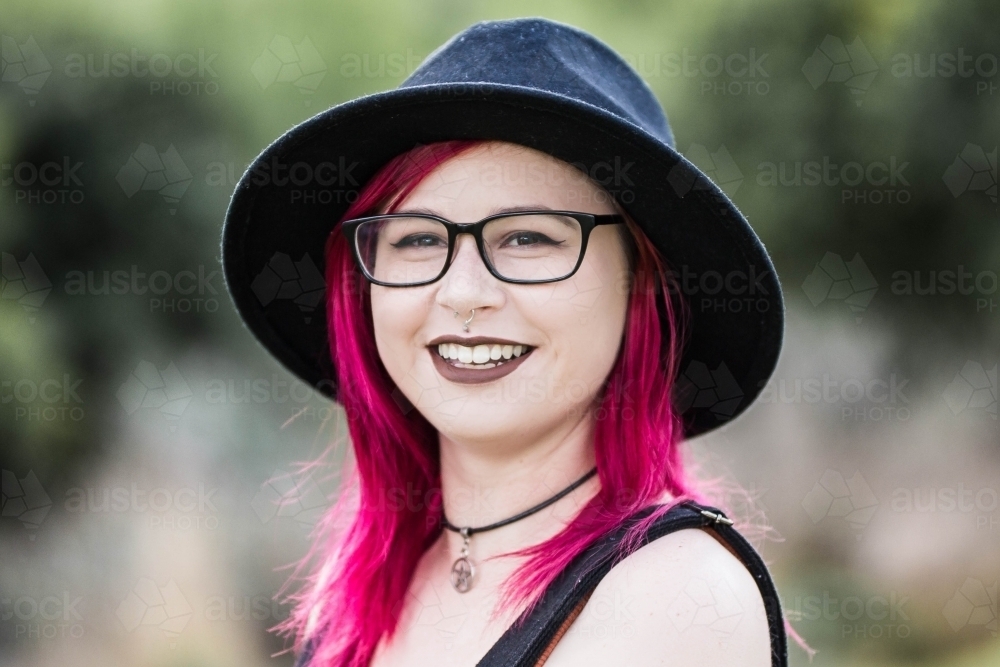 Young woman with lip piercing pink hair and glasses smiling - Australian Stock Image