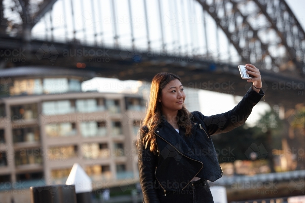 Young woman with mobile phone in front of harbour bridge - Australian Stock Image