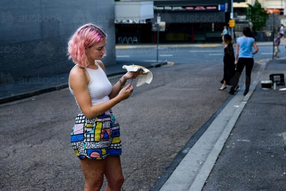 Young woman with pink hair doing embroidery in the street - Australian Stock Image