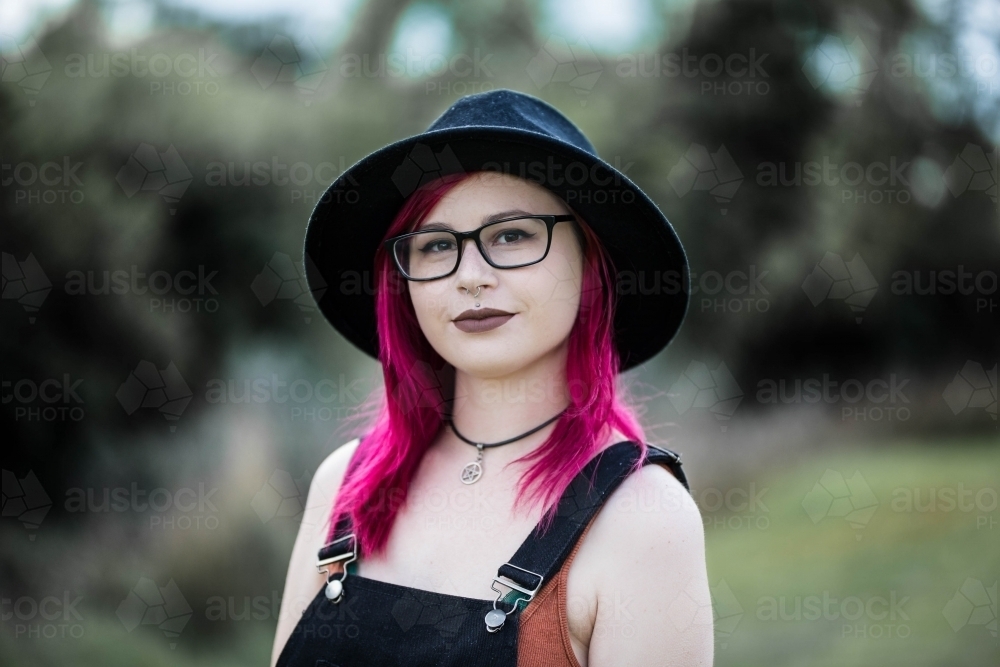 Young woman with pink hair glasses and hat looking serious - Australian Stock Image