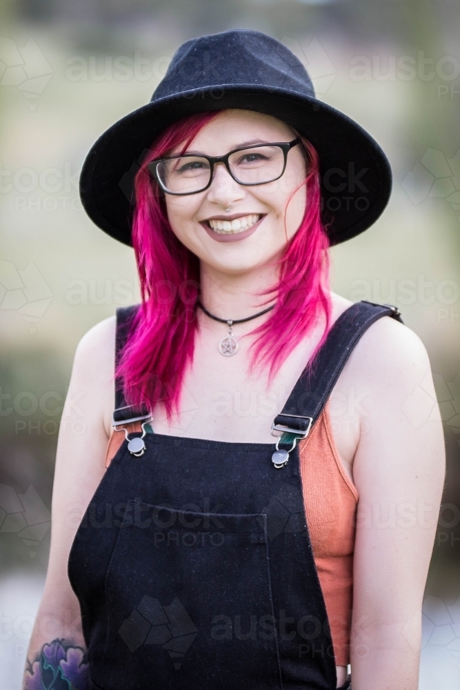 Young woman with pink hair glasses and hat smiling - Australian Stock Image