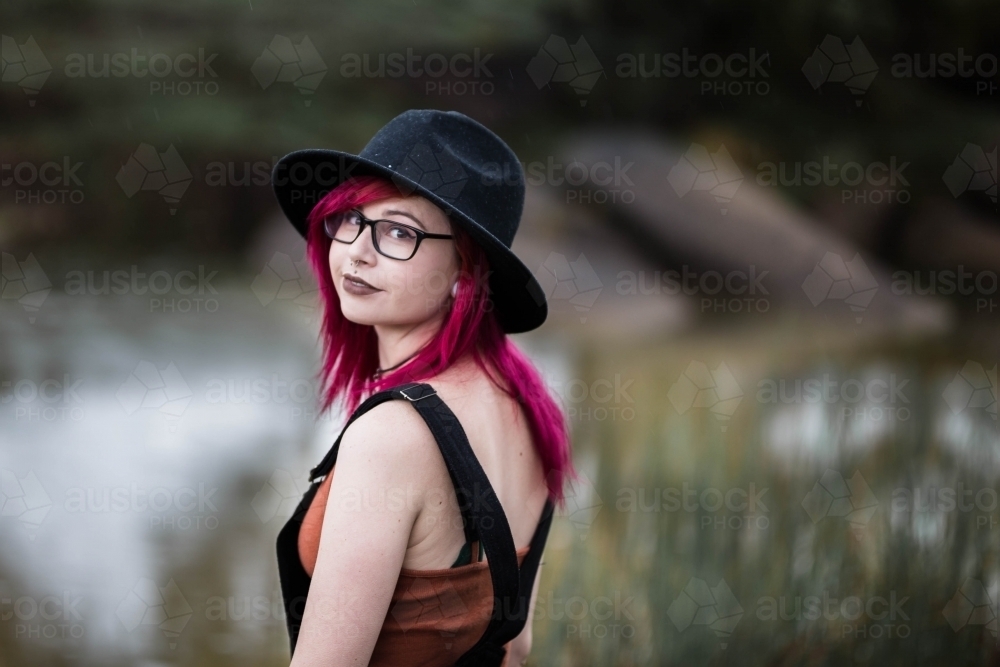 Young woman with pink hair hat and glasses looking over shoulder - Australian Stock Image