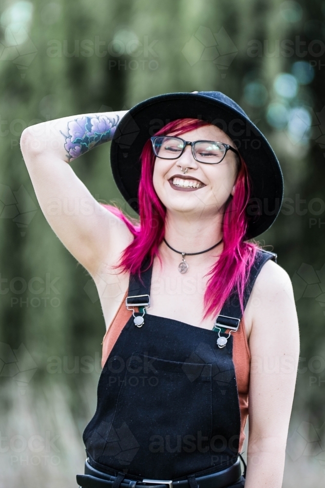 Young woman with pink hair holding onto hat laughing - Australian Stock Image