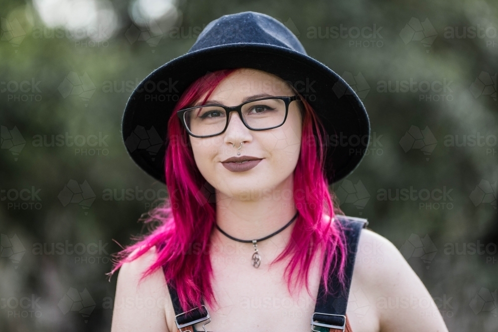 Young woman with pink hair smiling shyly - Australian Stock Image
