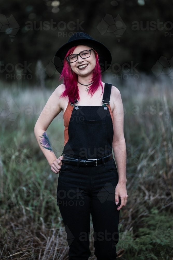Young woman with pink hair standing in long grass smiling - Australian Stock Image