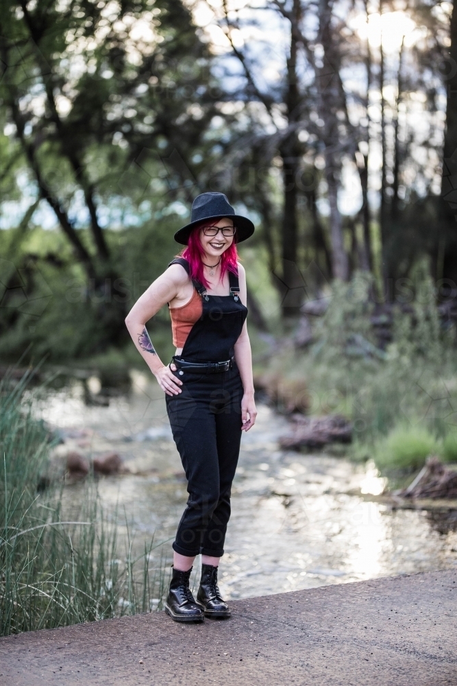 Young woman with pink hair standing near river water laughing - Australian Stock Image