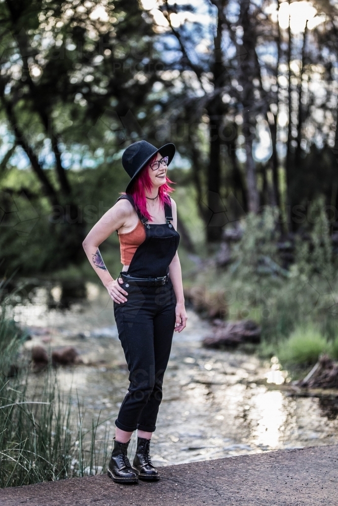 Young woman with pink hair standing near river water looking away laughing - Australian Stock Image