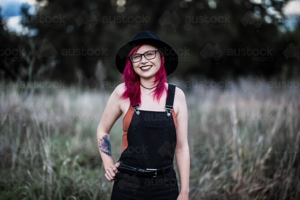 Young woman with pink hair standing smiling with hand on hip - Australian Stock Image