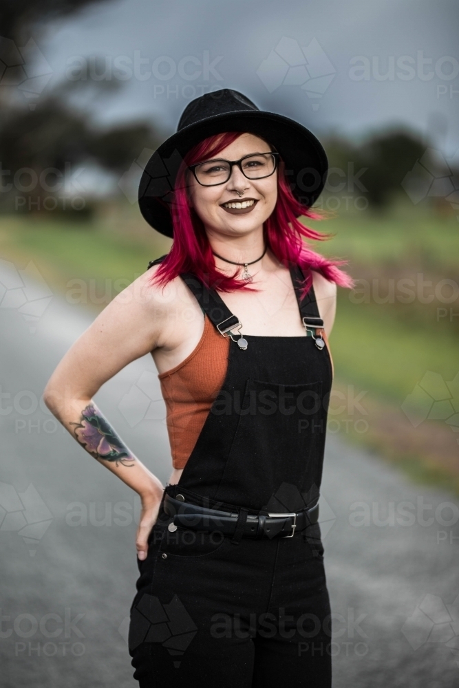 Young woman with pink hair standing with hands on hips smiling - Australian Stock Image