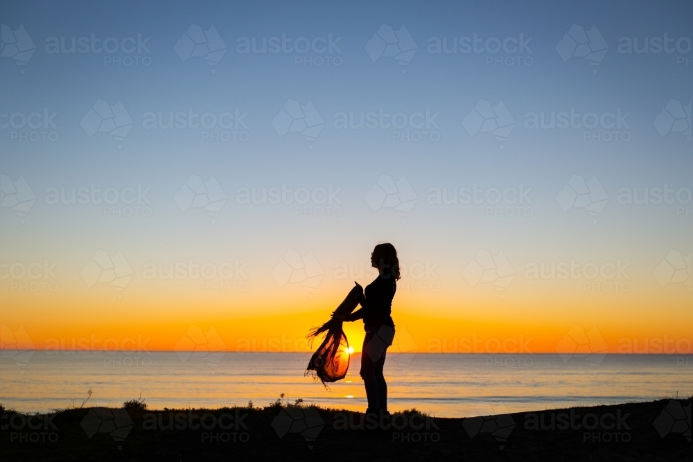 Young woman with scarf silhouetted against seaside sunset - Australian Stock Image