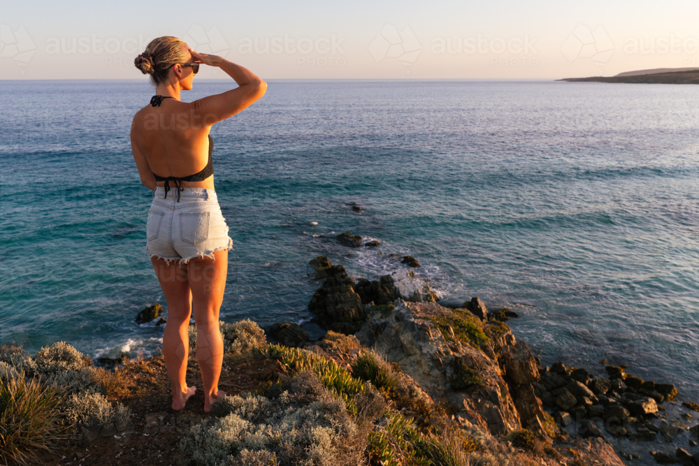 Young woman with view of ocean and desert coastline at sunset in South Australia - Australian Stock Image